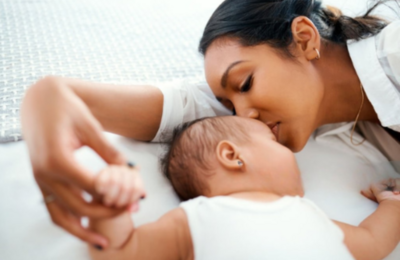 baby and mom laying on bed with mom kissing baby's forehead
