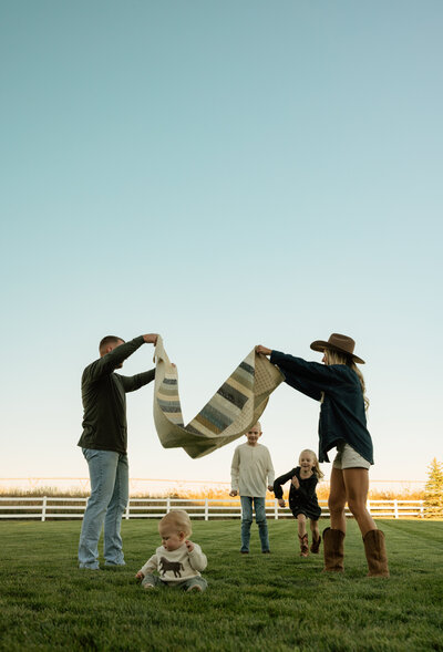 A family of 4 on a bridge, in a park in Rexburg, ID candidly smiling.