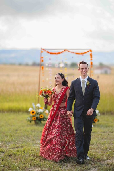 A bride wearing a red traditional Indian gown and groom walking away from the alter at the end of their wedding ceremony