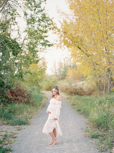 Pregnant mother snuggling baby bump in beautiful park during the fall in Edmonton