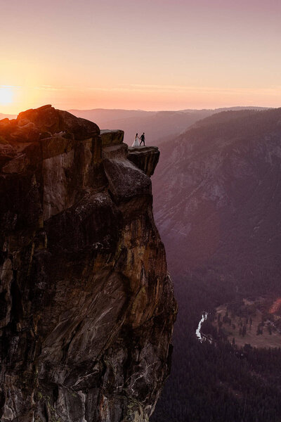 A bride and groom approach the edge the giant granite cliff at Taft Point, in Yosemite, during sunset.