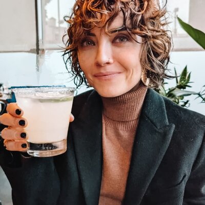 a wavy haired woman, holding a glass, smiling at the camera