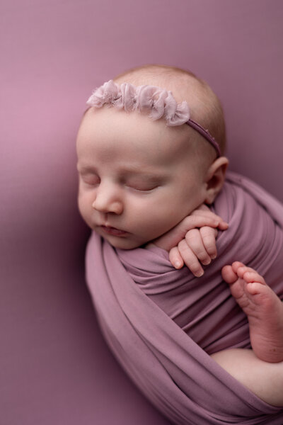 Newborn wrapped in soft pink blanket with adorable headband