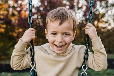 A smiling child holding onto swing chains in a park, captured by a Pittsburgh photographer.