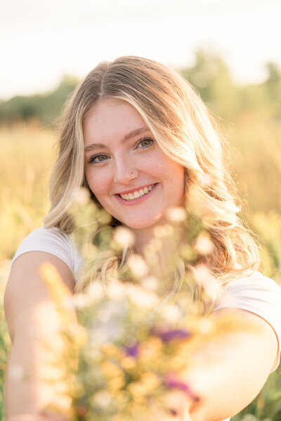 senior girl holds wildflowers towards camera and smiles, Indianapolis senior photographer