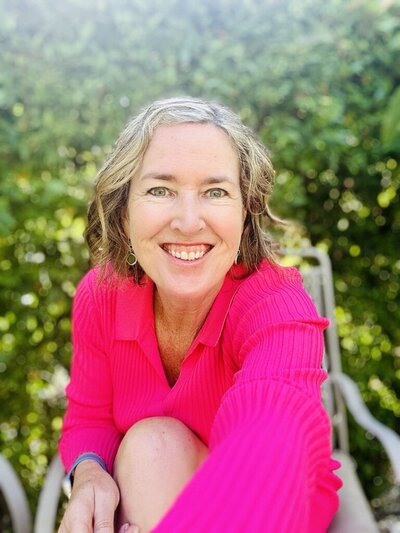 Laura Kate McHugh smiling and reaching forward, offering a warm, inviting presence and support for personal transformation