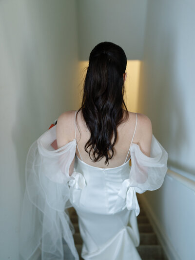 Bride in a satin gown with flowing sleeves walking down a staircase