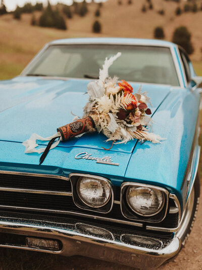 Close-up of a bridal bouquet resting on top of a vintage blue classic car.