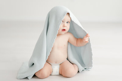 a baby peeks out from under a blue blanket 