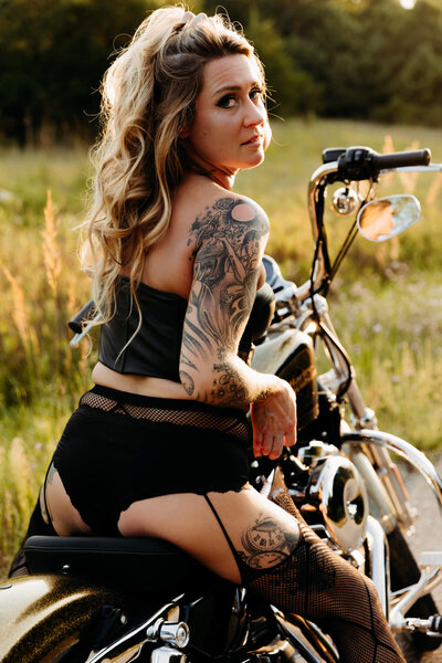 glamorous woman sitting on her motorcycle and looking back as she plays with her tights at sunset