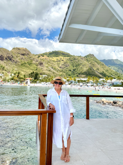 Woman in hat standing on deck over crystal clear water with mountains and tropical beach in background