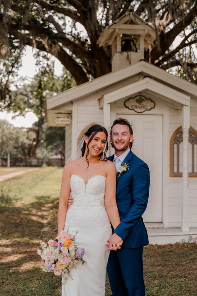 Bride and Groom smile at the camera outside while holding hands.