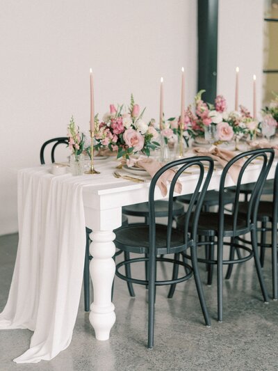 Beautiful wedding tablescape with pink flowers, candles, and black chairs