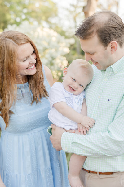 Baby grinning and showing his two teeth while parents smile down at him by Newborn Photographer Greenville