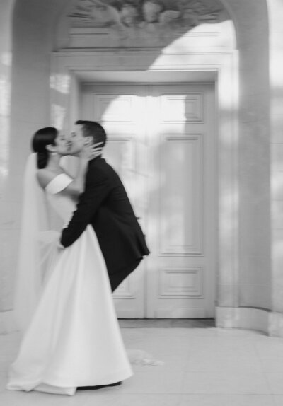 A bride and groom kiss outside a château in France in a Paris destination wedding, shot with a motion blur and black and white film aesthetic by Stacey Vandas.