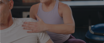 woman in purple tank top adjusting a man's shoulder on a pilates reformer 