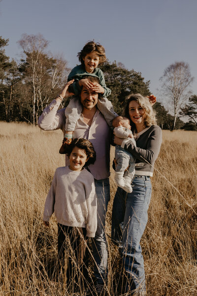 Een familieportret in een uitgestrekt veld, met blije gezichten en een natuurlijke achtergrond.