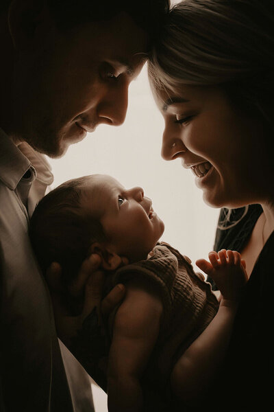 a silhouette of a mom and dad looking down at heir baby boy 