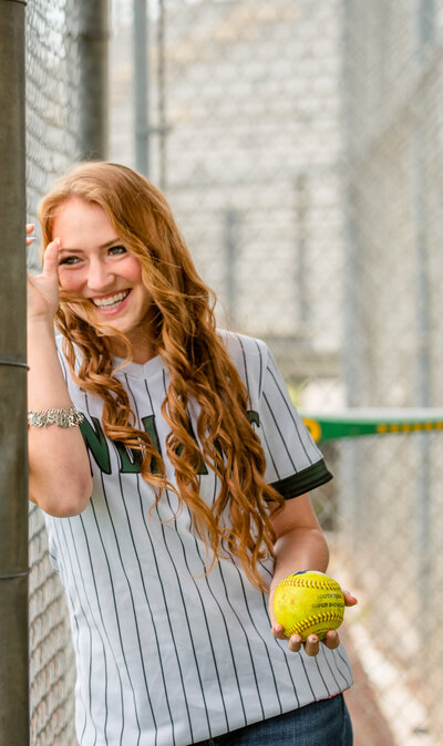 Houston grad photography session with softball player leaning against fence and smiling