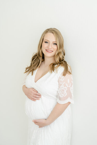 Mom in white dress in studio holding pregnant belly by Louisville maternity photographer