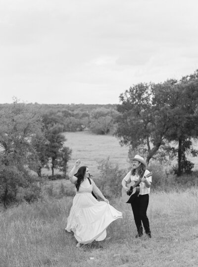 Black and white photo of Mikaela Kahn and her husband playing live music in a field