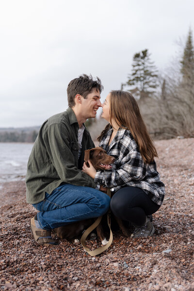 A couple gazes into each other’s eyes while holding their sweet puppy, capturing a joyful moment as they announce their engagement.