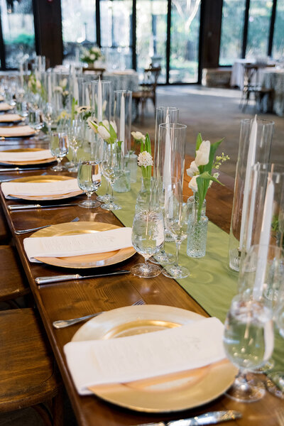 wooden table with gold plates and white napkins lined with a green table runner and vases of tulips
