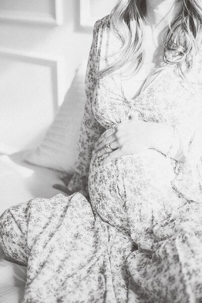 A pregnant woman is sitting on a bed in a black and white photo.