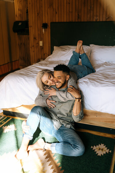 couple cuddle on side of bed laughing