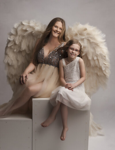 mother and child sitting for posed portrait in studio wearing couture feather wings in tan and white tan clothing near dupont