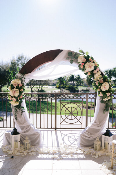 Floral-decorated wedding arch with lanterns, set up on a terrace with garden views