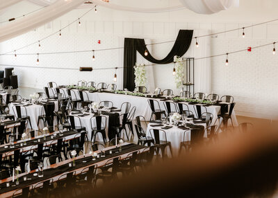 Interior of the August House venue in Dickinson, North Dakota, showing a spacious white-walled wedding reception hall with high ceilings, large windows, minimalist decor, and modern chandelier lighting.