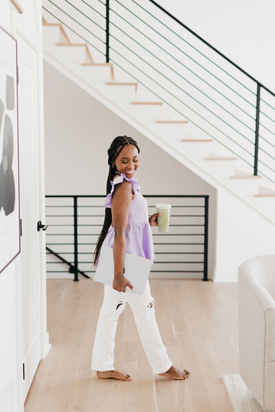 Juma Waganda walking in a purple top and white pants holding a laptop and matcha