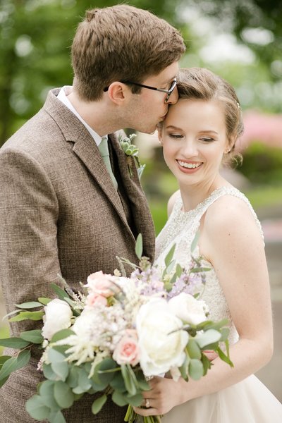 Bride holding a beautiful bouquet of flowers kissing her groom