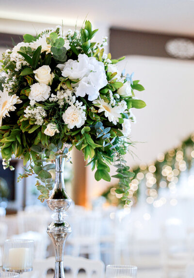 Tall wedding centerpiece featuring a sleek silver vase with lush white florals, creating an elegant and sophisticated tablescape, designed by In Full Bloom Event Planning & Design