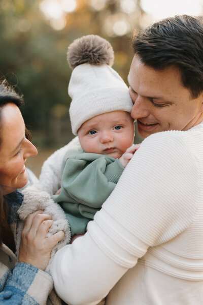 Baby wearing beanie looking at camera while being held by father