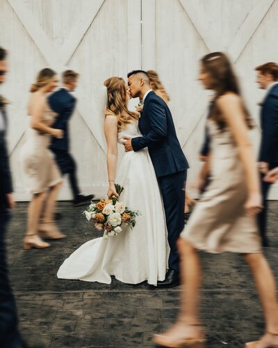 Bride and groom kissing with blurred people walking past