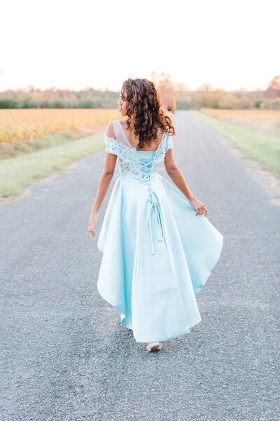 Woman wearing blue dress walking down a road, away from the camera