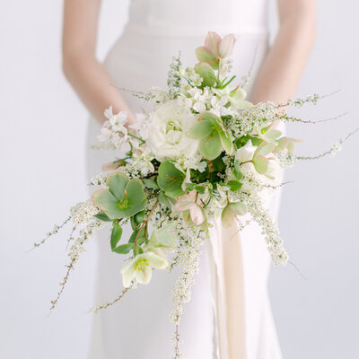 A bride holds an elegant bouquet of green and white flowers in a Montreal studio.
