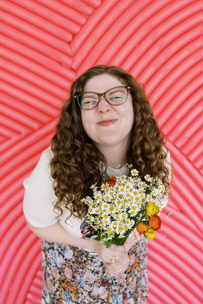 Allison Bolin Texas wedding photographer holding wildflowers in front of a pink striped wall