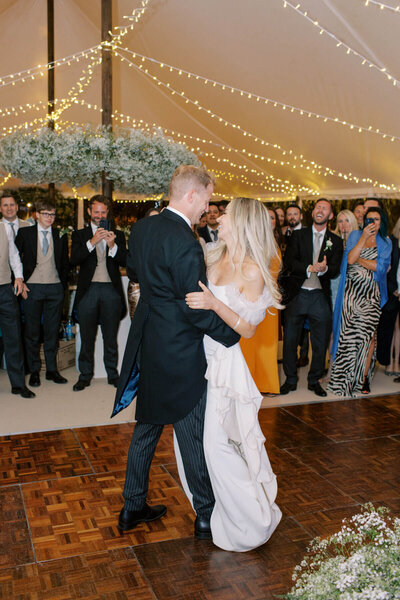 bride and groom first dance in the white marquee and beautiful string lights and white baby breath flower arrangements on floor and around bar area
