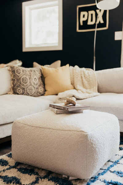 A oversized cream colored couch with decorative throw pillows and a ottoman in front of it and books stacked on top of it.