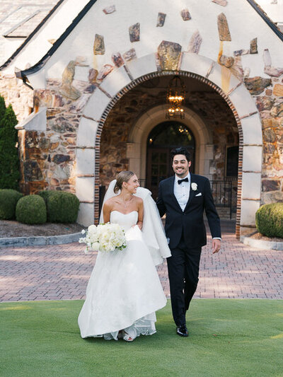 Bride and groom walking in front of Capitol City Club in Atlanta while the groom holds her veil