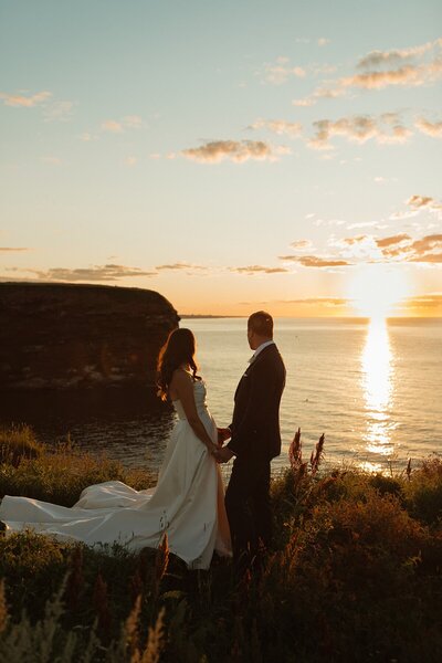 bride and groom hold hands next to ocean sunset for elopement photos in pei