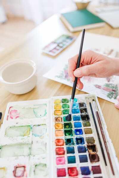 close up of an artist dipping her brush into a paint palette