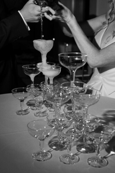 Two people pouring champagne over the top of a tower of glasses 