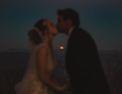 Bride and Groom on their elopement day kissing with the moon and mountains in the background.