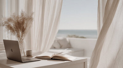 A minimalist neutral-toned workspace with a laptop, pampas grass, and soft sunlight, representing the calm and intentional design aesthetic of Kathalyst Design Studio.