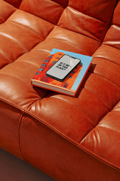 leather couch with bright orange book and a phone reading "Is it me or this place?"