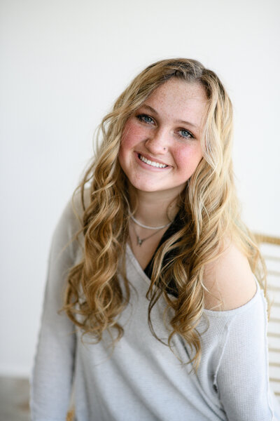 senior photo of a girl with long blonde curls and blue eyes smiling at the camera in a white studio setting